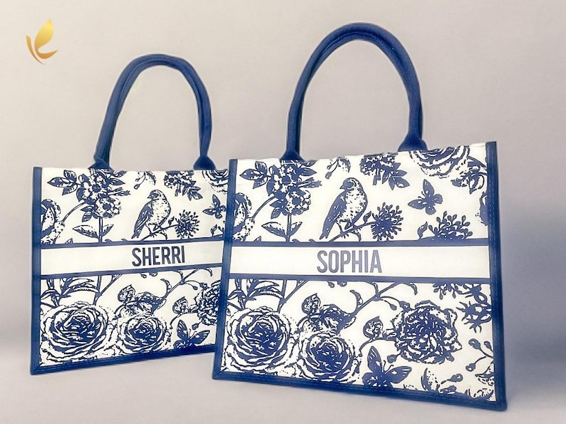 May include: Two blue and white tote bags with floral and bird designs. The bags have personalized names, "Sherri" and "Sophia", printed on the front.