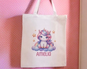 May include: White canvas tote bag with a colorful cartoon unicorn sitting on a cloud with stars and a rainbow. The bag has the name Amelia printed on it.