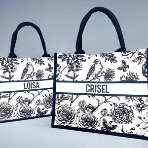 May include: Two black and white tote bags with floral and bird designs. The bags have black handles and a white stripe with the names 'Loisa' and 'Crisel' printed on them.