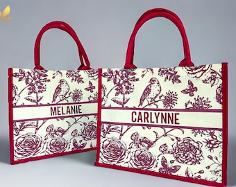 May include: Two red tote bags with white fabric and a floral print in burgundy. The bags have a white stripe with the names "Melanie" and "Carlynne" printed on them.