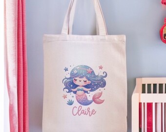 May include: A white tote bag with a cartoon mermaid illustration and the name "Claire" printed on the front. The mermaid has blue hair, a pink tail, and is surrounded by stars.