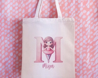 May include: A white canvas tote bag with a pink letter M and a ballerina illustration. The name "Miya" is printed below the letter.