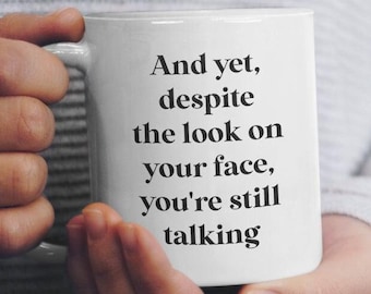 May include: White ceramic mug with black text that reads "And yet, despite the look on your face, you're still talking."