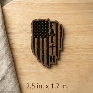 May include: A wooden cutout featuring an American flag design with the word "FAITH" vertically displayed. The cutout measures 2.5 inches by 1.7 inches. The flag's stars and stripes are visible, and the word "FAITH" includes a cross.
