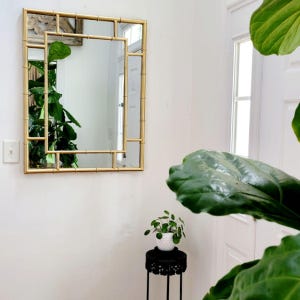 May include: A rectangular wall mirror featuring a gold-toned frame designed to resemble bamboo stalks. The frame consists of a central rectangular glass pane surrounded by a secondary outer frame structure, creating a layered geometric appearance.