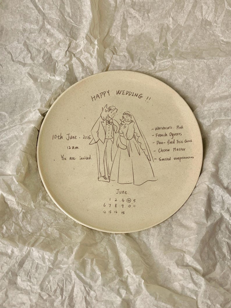 Peut inclure: Une assiette ronde en c&eacute;ramique blanc cass&eacute; avec un dessin au trait noir repr&eacute;sentant un couple de mari&eacute;s. Le texte inclut 'HAPPY WEDDING !!', '10th June 2025', '12 a.m.', 'You are invited.', un menu et un calendrier de juin avec le 4 entour&eacute;.