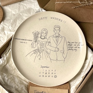 May include: A round, off-white ceramic plate featuring a black line-art illustration of a couple in wedding attire. The text reads HAPPY WEDDING!!, ZHENZHECHEN&CAIXIAOMENG 2025.09.17, a calendar for September with the 17th circled, and a written message.