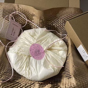Peut inclure: Un paquet rond envelopp&eacute; dans du papier de soie cr&egrave;me, fix&eacute; par un autocollant rose repr&eacute;sentant un ours en dessin anim&eacute; avec le texte Happy Birthday. Une ficelle rose entoure le paquet, accompagn&eacute; d'une &eacute;tiquette marqu&eacute;e Sweet dream.