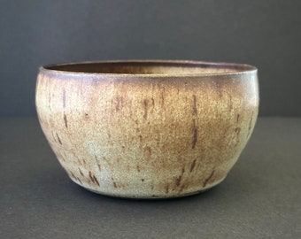 May include: A brown and beige ceramic bowl with a speckled glaze. The bowl has a rounded shape and a slightly flared rim.