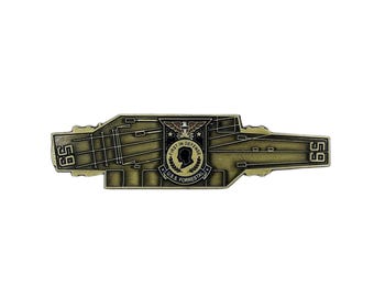 May include: A gold-colored metal pin in the shape of a U.S. Navy aircraft carrier. The pin features the number "59" on both ends and a central emblem with the text "FIRST IN DEFENSE" and "U.S.S. FORRESTAL".