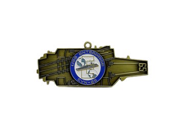 May include: A bronze-colored metal USS Enterprise CVN-65 aircraft carrier shaped ornament. The center features a blue circle with the ship's name and a graphic of the ship. The number 65 is on the right side.