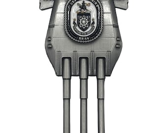 May include: A silver-toned metal pin shaped like a battleship gun turret with three barrels. It features the text 1944 and 1991 on the sides and a central emblem with the text USS WISCONSIN, FORWARD FOR FREEDOM, and BB 64 in black and white.
