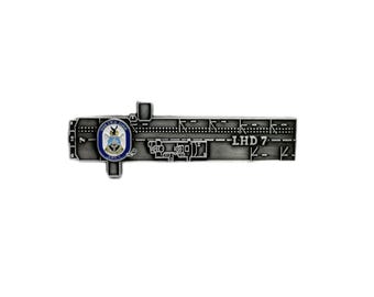 May include: A silver-colored metal pin featuring a detailed design of a ship's deck plan. The pin includes a circular emblem with a blue and white border and the text "USS Iwo Jima". The text "LHD 7" is also visible.