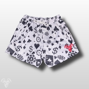 May include: White athletic shorts with a black and white print of playing cards, dollar signs, and stars. The shorts have a red logo on the right side.