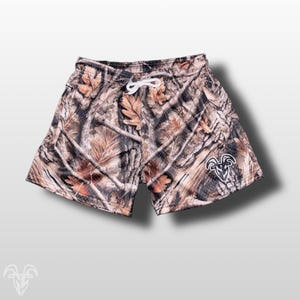 Könnte beinhalten: Shorts mit Camouflage-Print und weißem Kordelzug. Die Shorts haben ein Muster aus Braun, Beige und Schwarz mit einem weißen Logo auf der unteren rechten Seite. Die Shorts sind für Komfort und Outdoor-Aktivitäten konzipiert.