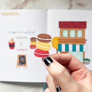 May include: A stack of three colorful macarons, with a red, yellow, and brown macaron, on a white background. The macarons are a popular French pastry.
