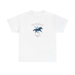 Op de afbeelding: Wit t-shirt met een blauwe afbeelding van een paard in een ster, met de tekst "Old Recliners Ranch" en "EST 1957". Het ontwerp is gecentreerd op de voorkant van het shirt.