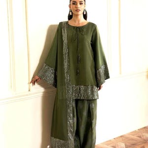 May include: Olive green ensemble featuring a long-sleeved top with a tie neckline and wide sleeves, paired with matching pants. The outfit is accented with silver sequin trim on the sleeves, hem, and scarf. The outfit is a traditional style.