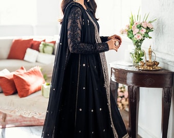 May include: A floor-length black dress featuring long sheer sleeves with intricate embroidery, a matching dupatta draped over the shoulder, and gold metallic detailing along the hemline and front edges, accented with small scattered floral motifs.