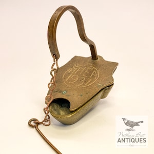 May include: Antique brass oil lamp with a handle and chain. The lamp has a hinged lid and a small bowl for oil. The top of the lamp is stamped with the letters "AHEA" and the year "1937".