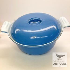 May include: A bright blue enameled metal casserole dish with a matching lid. The pot features two white side handles with a ribbed texture and a white rim. There is visible wear and minor chipping along the edges of the rim and the handles.