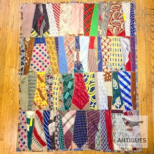 Op de afbeelding: Een patchworkquilt gemaakt van diverse patronen stropdassen. De quilt heeft een verscheidenheid aan kleuren en ontwerpen, waaronder stippen, strepen en geometrische patronen. De stropdassen zijn in verticale rijen gerangschikt, wat een uniek en kleurrijk textiel creëert.