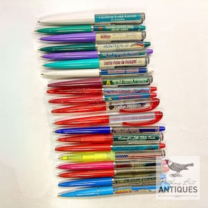 May include: A collection of vintage souvenir pens with various colored barrels and clear plastic sleeves. Each pen features a different location name, including "Chateau Lake Louise Canada" and "Grand Canyon Arizona."