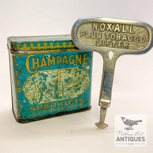 Puede incluir: Una lata antigua de Champagne Sparklets de color turquesa y dorado con un levantador de tabaco Noxall Plug de metal. La lata presenta la palabra "Champagne" y una ilustración de botella. El levantador tiene el texto "NOXALL PLUG TOBACCO LIFTER".
