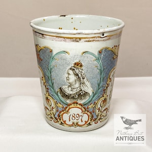 Puede incluir: Taza antigua de esmalte blanco con un retrato de la reina Victoria, enmarcado por adornos azules y dorados. El año 1897 está visible debajo del retrato. La taza presenta un ligero desgaste, lo que le da un encanto vintage.
