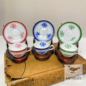 Puede incluir: Conjunto de tres tazas de té en miniatura y platillos con diseños florales. Las tazas y los platillos son blancos con ribetes dorados y presentan diferentes patrones florales de colores: rosa, azul y verde.