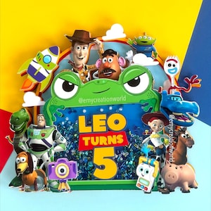 May include: A vibrant birthday cake decoration featuring Toy Story characters. The design includes Woody, Buzz Lightyear, and other characters, with the text "LEO TURNS 5" in yellow and red. The background is a mix of blue, yellow, and green.