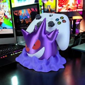 May include: A purple 3D-printed Gengar figure with red eyes and a wide grin, holding a white Xbox controller. The figure sits on a purple cloud-like base, perfect for gamers.