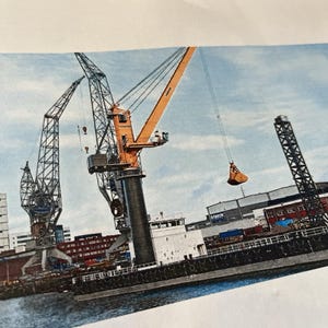 May include: A harbour scene with a cargo ship and several cranes. The cranes are orange and black, with one lifting a bucket. Buildings and a cloudy sky are in the background. The ship is black and white.
