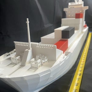 May include: A white model cargo ship with red and black containers. The model is approximately 40 inches long, with detailed features including a mast, deck machinery, and a bridge. The ship is set against a dark background.