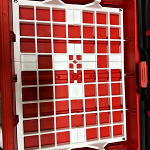 May include: A white plastic grid organizer insert placed inside a red rectangular tool box. The grid features a repeating square pattern and is labeled with the letters A, B, C, and D at each of its four corners to assist with orientation.