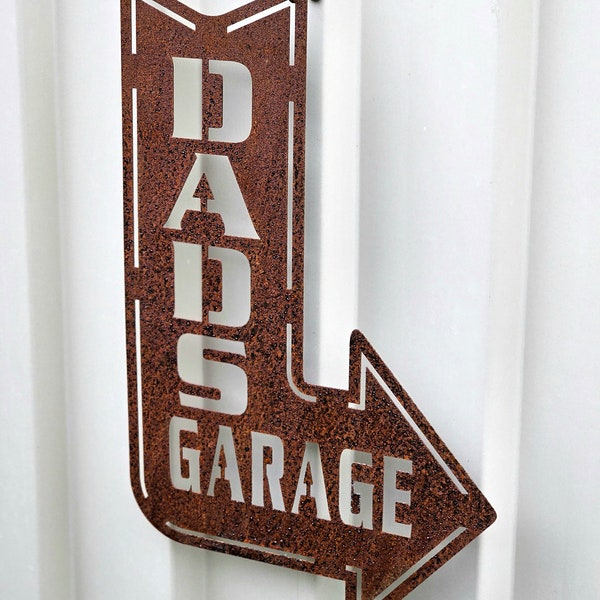 Könnte beinhalten: Rostfarbener Pfeil aus Metall mit der Aufschrift "Dad's Garage" in weißen Buchstaben.