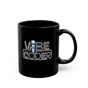 May include: A black ceramic mug featuring a white outlined graphic that spells out the text VIBE CODER. The letter I in VIBE is replaced by a blue and white illustration of a microphone with an electrical plug attached to the base of the handle.