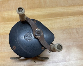 Puede incluir: Un carrete de pesca negro con una manija blanca y una manivela de metal. El carrete tiene una etiqueta que dice "Viking No. 1301".