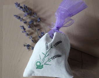 May include: A white fabric pouch with a lavender design and a purple ribbon. The pouch is filled with dried lavender flowers.
