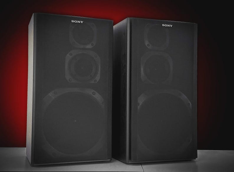 Puede incluir: Dos altavoces negros Sony con m&uacute;ltiples componentes de altavoz. Los altavoces tienen forma rectangular y est&aacute;n colocados uno al lado del otro. El logotipo de Sony es visible en la parte superior de cada altavoz.