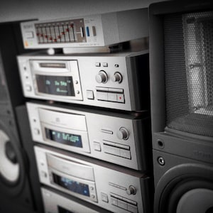 Puede incluir: Una pila de componentes de audio plateados vintage, que incluyen un reproductor de CD, una pletina de casete y un amplificador, con un ecualizador gr&aacute;fico en la parte superior. Un gran altavoz negro est&aacute; a la derecha. Los componentes tienen botones y pantallas.