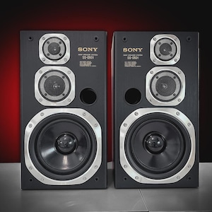 Puede incluir: Dos altavoces negros Sony SS-0501 con detalles plateados. Cada altavoz tiene un woofer central grande, dos altavoces m&aacute;s peque&ntilde;os y un puerto circular. Fondo degradado de rojo oscuro a negro.
