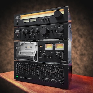 以下が含まれることがあります： チューナー、アンプ、カセットデッキ、グラフィックイコライザーなど、黒色のヴィンテージオーディオ機器のスタック。木製の表面に配置され、さまざまなノブ、ダイヤル、メーターが見えます。背景は茶色と黒のグラデーションです。