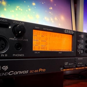 May include: Black electronic music synthesizer with an orange display showing instrument settings. The device has various buttons, knobs, and ports, including "MIDI IN B" and "PHONES." The brand name "EDIROL" is visible.