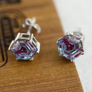 Puede incluir: Un par de pendientes de plata con una piedra preciosa hexagonal iridiscente en cada uno. Las piedras preciosas son una mezcla de azul, morado y rosa.