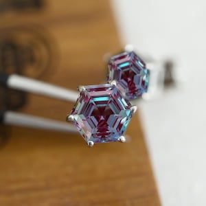 May include: A pair of silver stud earrings featuring iridescent hexagonal gemstones. The gemstones display a purple, blue and green colour.