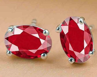 Peut inclure: Une paire de boucles d'oreilles à clous avec des pierres précieuses rouges taillées en forme ovale. Les pierres sont serties dans un métal argenté avec quatre griffes arrondies. Les boucles d'oreilles sont présentées sur une surface de couleur neutre.