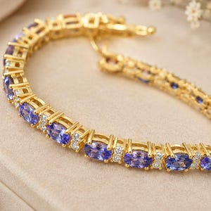 Può includere: Un bracciale tennis color oro caratterizzato da una serie di pietre preziose tanzanite viola a taglio ovale alternate a piccole pietre d'accento trasparenti a taglio rotondo. Il bracciale presenta una montatura a maglie e una chiusura.