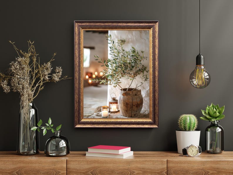 May include: A framed print of a still life featuring a rustic pot with a small olive branch, a lantern, and candles. The frame is brown with gold accents.