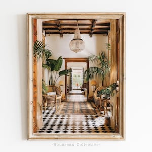 May include: A view through a wooden doorway into a room with a black and white chequered floor, two wicker chairs, and a chandelier hanging from the ceiling. The room is decorated with plants and has a wooden door at the far end.